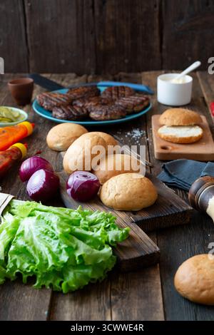 Vorbereitung auf hausgemachte Grillgerichte. Frische Burger-Zutaten und gegrillte Pasteten auf rustikalem Tisch, fertig zum Kochen. Stockfoto