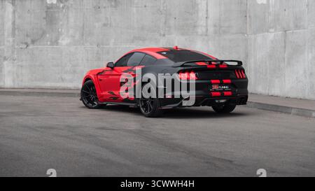 Rot-schwarzer Ford Mustang auf einer Straße. Hintere Dreiviertelansicht eines amerikanischen Ponywagens, das an einer Betonmauer geparkt ist. Stockfoto