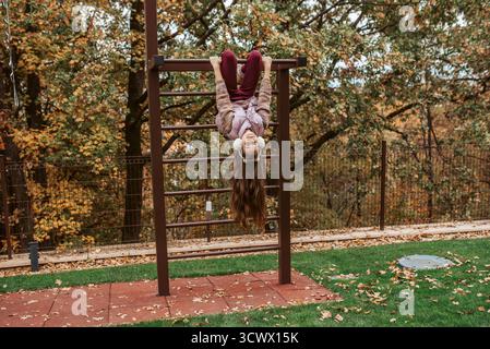 Mädchen hängt kopfüber auf Spielplatz-Affenstangen. Stockfoto