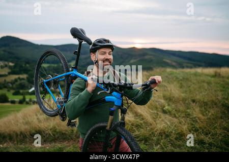 Radfahrer, der Fahrrad auf der Schulter in der Natur trägt. Stockfoto
