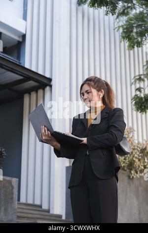 Eine Frau im Business-Anzug hält einen Laptop und einen Ordner in der Hand Stockfoto