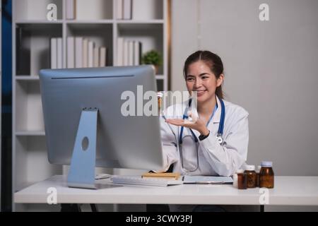 Eine Frau in einem weißen Labormantel sitzt an einem Schreibtisch vor einem Computermonitor Stockfoto