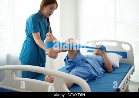 Eine Frau in blauer Uniform hilft einem Mann in einem Krankenhausbett Stockfoto