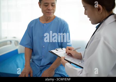 Eine Ärztin schreibt vor einem älteren Mann auf eine Zwischenablage Stockfoto