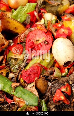 Eine lebhafte Nahaufnahme eines Kompostbehälters, der mit organischen Abfällen und Lebensmittelresten für das Recycling gefüllt ist. Der Haufen enthält eindeutig eine rote Tomate und Stockfoto