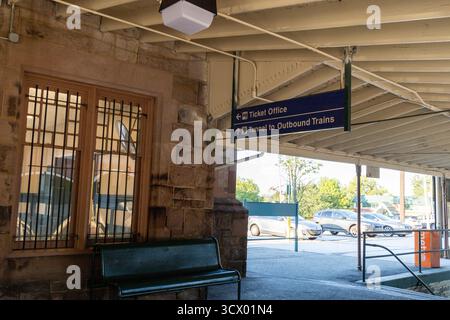 Ein Bahnhof Devon mit einem blauen Schild mit der Aufschrift „Travel Center“. Es gibt eine Bank vor dem Bahnhof und ein paar Autos parken auf dem Parkplatz, Philade Stockfoto