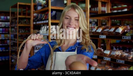 Der Angestellte im Geschäft trägt eine leichte Schürze und bietet frisches Ei im Supermarkt an, mit Korbkorb in der Nähe von Regalen Stockfoto