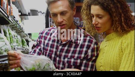 Einkäufer in kariertem Hemd und gelbem Pullover überprüfen versiegelte Salatbeutel im Gang von Lebensmittelprodukten Stockfoto