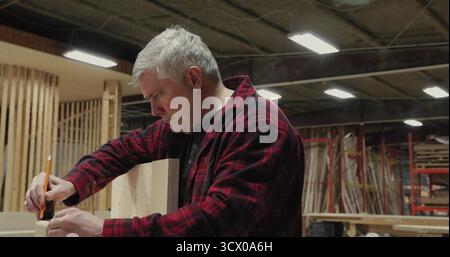 Zimmermann mit Flanell, der Holzdiele an der Werkbank in der Holzwerkstatt markiert, mit Bleistift und Quadrat Stockfoto