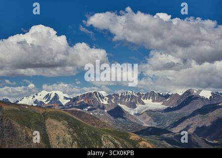 Schneebedeckte Berge erheben sich majestätisch gegen einen tiefblauen Himmel voller flauschiger Wolken während der Sommersaison. Die Szene fängt die Schönheit der Natur ein Stockfoto