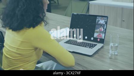 Sitzende hispanische Frau, die am Konferenztisch auf einem Laptop schreibt, mit Papieren und klarem Glas Wasser Stockfoto