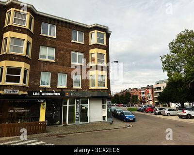 Lüttich, Belgien - 20. Oktober 2023: Backsteingebäude in Lüttich Belgien beherbergt Geschäfte und eine Apotheke mit geparkten Autos entlang der Straße. Stockfoto