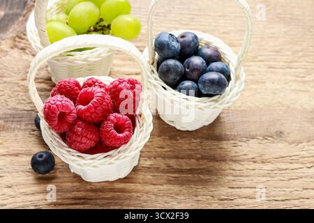 Baskets with fruits: raspberry, blueberry and grapes. Wooden background. Stockfoto