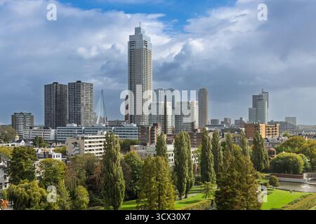 Ein Panoramablick auf die Rotterdamer Skyline, mit einer Mischung aus modernen Wolkenkratzern und umliegenden grünen Parkflächen unter einem dramatischen bewölkten Himmel, hochgradig Stockfoto