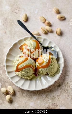 Pistazieneis und Löffel auf beigefarbenem Teller, dekoriert mit Karamellsauce Stockfoto