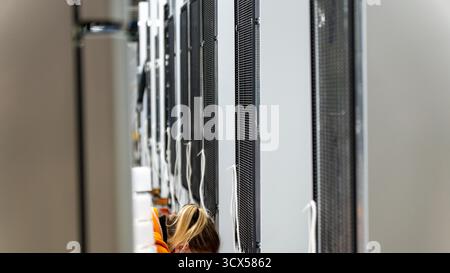 Eine Frau arbeitet in einem Rechenzentrum und konzentriert sich auf die dichten Reihen von Server-Racks. Das Bild erfasst die moderne Infrastruktur und die menschlichen Elemente Stockfoto