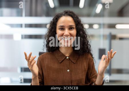 Junge Frau lächelt in die Kamera, führt ansprechende Gespräche während der Online-Videokonferenz, drückt Glück und Optimismus in einer modernen Unternehmensumgebung aus Stockfoto