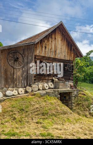 Altes Holzhaus auf einem Hügel mit Mühlsteinen und Wagenrädern, die das Äußere schmücken Stockfoto