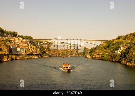 Bootstour auf dem Fluss Douro unter der Arrábida-Brücke in Porto, Portugal, an einem sonnigen Nachmittag mit Blick auf die Stadt und goldenem Licht. Stockfoto
