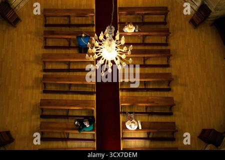 Blick von oben auf die Menschen, die in einer Kirche sitzen, beleuchtet von einem großen Kronleuchter, die eine ruhige und symmetrische Innenszene schaffen, Pontevedra, Galicien. Stockfoto