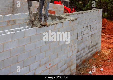 Der Bauarbeiter gießt während der Arbeit tagsüber Zement auf die zu bauende Wand, umgeben von Schmutzmaschinen Stockfoto