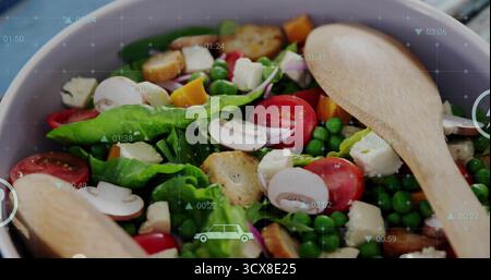 Graue Schüssel mit farbenfrohem Salat und Holzlöffeln auf der Arbeitsplatte mit digitaler Überlagerung Stockfoto