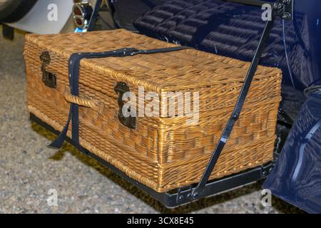 Ein Picknickkorb aus gewebtem Korb - Koffer an einem Metallgestell auf der Rückseite des Veteranenautos befestigt, bereit für einen Tagesausflug. Stockfoto