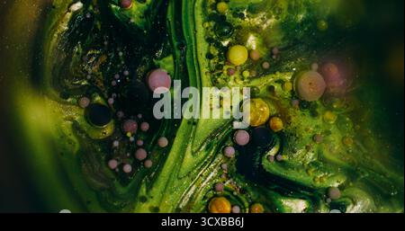 Unscharfe, glänzende Blasen. Bunte Tintenflüssigkeit. Grüne lila gelbe Glitzer runde Öltextur, die auf abstraktem Kunst-Bokeh-Hintergrund schwimmt. Stockfoto