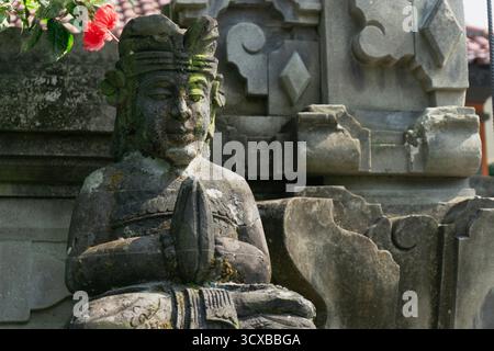 Diese Nahaufnahme des Kopfes und des Oberkörpers einer balinesischen Hindugottsstatue, bedeckt mit dickem Moos, vermittelt ein Gefühl von Alter und tiefem Kulturerbe Stockfoto
