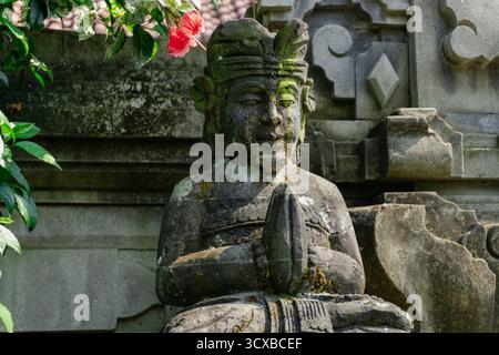 Diese Nahaufnahme des Kopfes und des Oberkörpers einer balinesischen Hindugottsstatue, bedeckt mit dickem Moos, vermittelt ein Gefühl von Alter und tiefem Kulturerbe Stockfoto