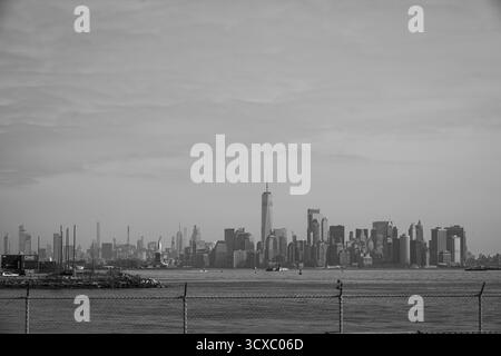 Bayonne, NJ, USA – 14. März 2025: Dramatisches Schwarz-weiß-Bild der Skyline von Manhattan mit der Freiheitsstatue im Vordergrund unter einem bewölkten s Stockfoto