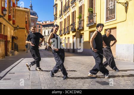 Gruppe von städtischen Tänzern in schwarzer Kleidung, die auf einer Kopfsteinpflasterstraße in madrid, spanien, eine zeitgenössische Tanzroutine vorführen und künstlerische Bewegungen und zeigen Stockfoto