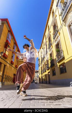 Mann tanzt energisch auf einer sonnigen Kopfsteinpflasterstraße in madrid, zeigt urbanen Stil und zeitgenössische Bewegung, Freiheit, Freude und selbstbewusste Straße Stockfoto