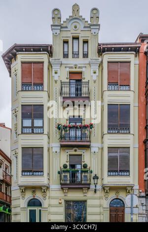 Detaillierte Ansicht einer verzierten, blassgelben eklektischen oder Novecentista-Fassade in Nordspanien mit einem zentralen dekorativen Turm und auskragenden Balkonen Stockfoto