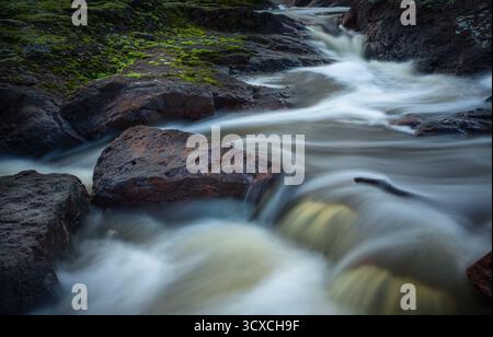 der creek fließt schnell über dunkle, glatte Felsen an den Nigretta Falls, Victoria. Das Wasser wirkt milchig, da es lange ausgesetzt ist, wodurch ein weicher, fließender Effekt entsteht Stockfoto