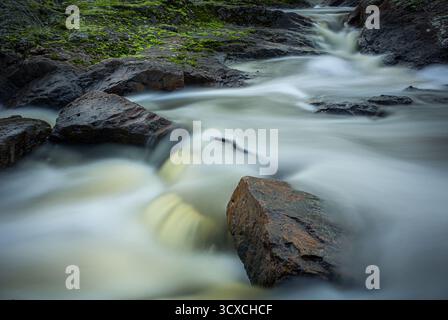 Ein Bach fließt sanft durch eine felsige Landschaft bei den Nigretta Falls, Victoria. Das Wasser erscheint milchig, mit langer Belichtung aufgefangen und windet sich um l Stockfoto