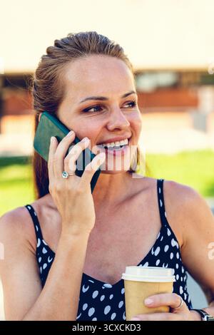 Frau in der Stadt, die auf dem Smartphone spricht, während sie Kaffee zum Mitnehmen hält Stockfoto