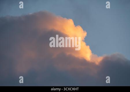 Der Rand einer dramatischen dunklen Wolke fängt das warme goldene Licht des Sonnenuntergangs ein und schafft einen schönen und hoffnungsvollen Hintergrund. Stockfoto