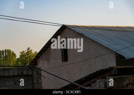 Teilweise errichtetes ländliches Gebäude mit abgeschrägtem Metalldach, Betonblockwänden und Versorgungsdrähten vor einem klaren Himmel Stockfoto