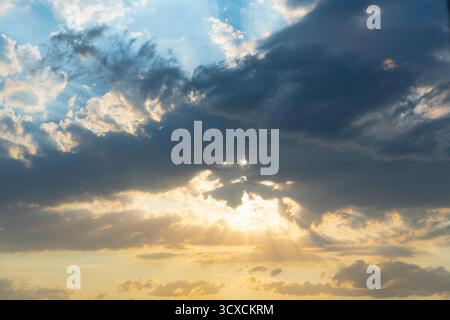 Goldenes Sonnenuntergangslicht, das durch dunkle Wolken strömt, erzeugt eindrucksvolle kammergetrocknete Strahlen in einer dramatischen Himmelsszene Stockfoto