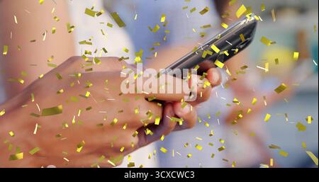Griffiges, braunhäutiges Smartphone in warmer Innenausstattung mit schwebendem goldenem Konfetti Stockfoto