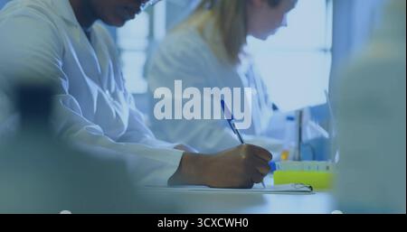 Dokumentieren Sie das Schreiben von afroamerikanischen Wissenschaftlern mit Stift auf Klemmbrett am Labortisch, Reagenzglasgestell Stockfoto
