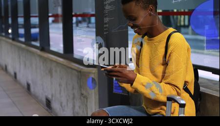 Smartphone in der Hand, Frau in Jeans auf Bahnhofsplattform mit Ohrstöpsel, Rucksack, Gepäckraum Stockfoto