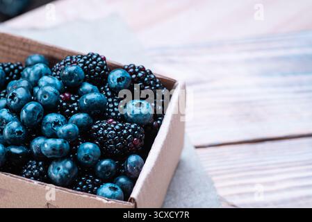 Heidelbeeren und Brombeeren in einem Karton auf einem Holztisch Stockfoto
