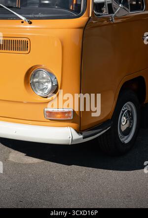 Vordere linke Ecke des alten orangefarbenen Van. Klassischer VW T2 Kleinbus an sonnigem Tag – Nahaufnahme von Scheinwerfer, Tür, Stoßfänger und Rad. Stockfoto