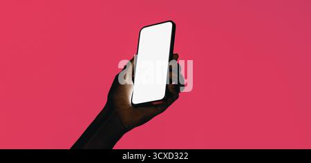 Ein Smartphone mit leerem Bildschirm wird von einer Hand vor einem leuchtend rosa Hintergrund gehalten und zeigt moderne Technologie und Möglichkeiten zum Kopieren. Stockfoto