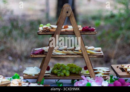 Catering-Einrichtung im Freien mit einem rustikalen dreistöckigen Stand mit verschiedenen Käsesorten, frischen Trauben und Beeren für die Gäste Stockfoto