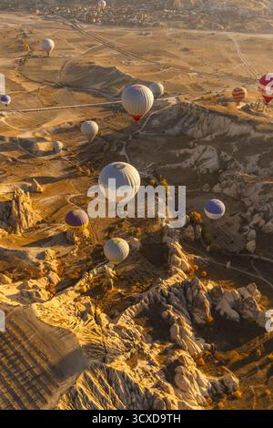 Kappadokien, Turkiye - 06. November 2022: Der Blick auf Heißluftballons schweigend über eine Landschaft aus goldfarbenen Felsformationen, die lange Schatten in das warme Morgenlicht werfen. Stockfoto