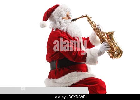 Der weihnachtsmann sitzt an einer Wand und spielt ein Saxophon isoliert auf weißem Hintergrund Stockfoto
