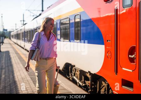 Schöne und elegante Geschäftsfrau, die mit Koffer am Bahnhof spaziert. Stockfoto
